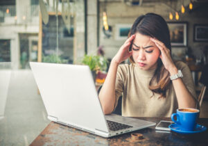 Young beautiful asian woman feeling hurt, fatigue, head ache, and stressed working with laptop in coffee shop cafe, vintage tone, office syndrome concept